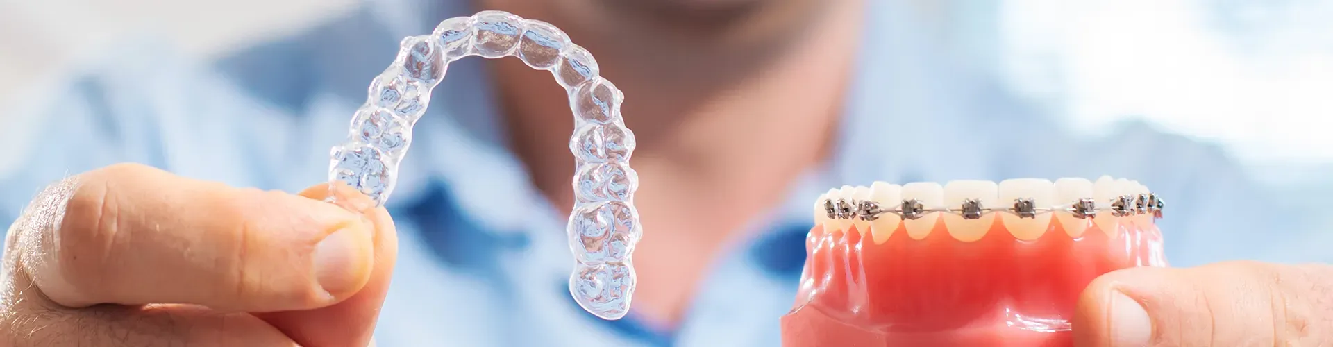 man holding clear aligners in one hand and a model of braces on teeth in the other