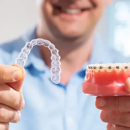 man holding clear aligners in one hand and a model of braces on teeth in the other